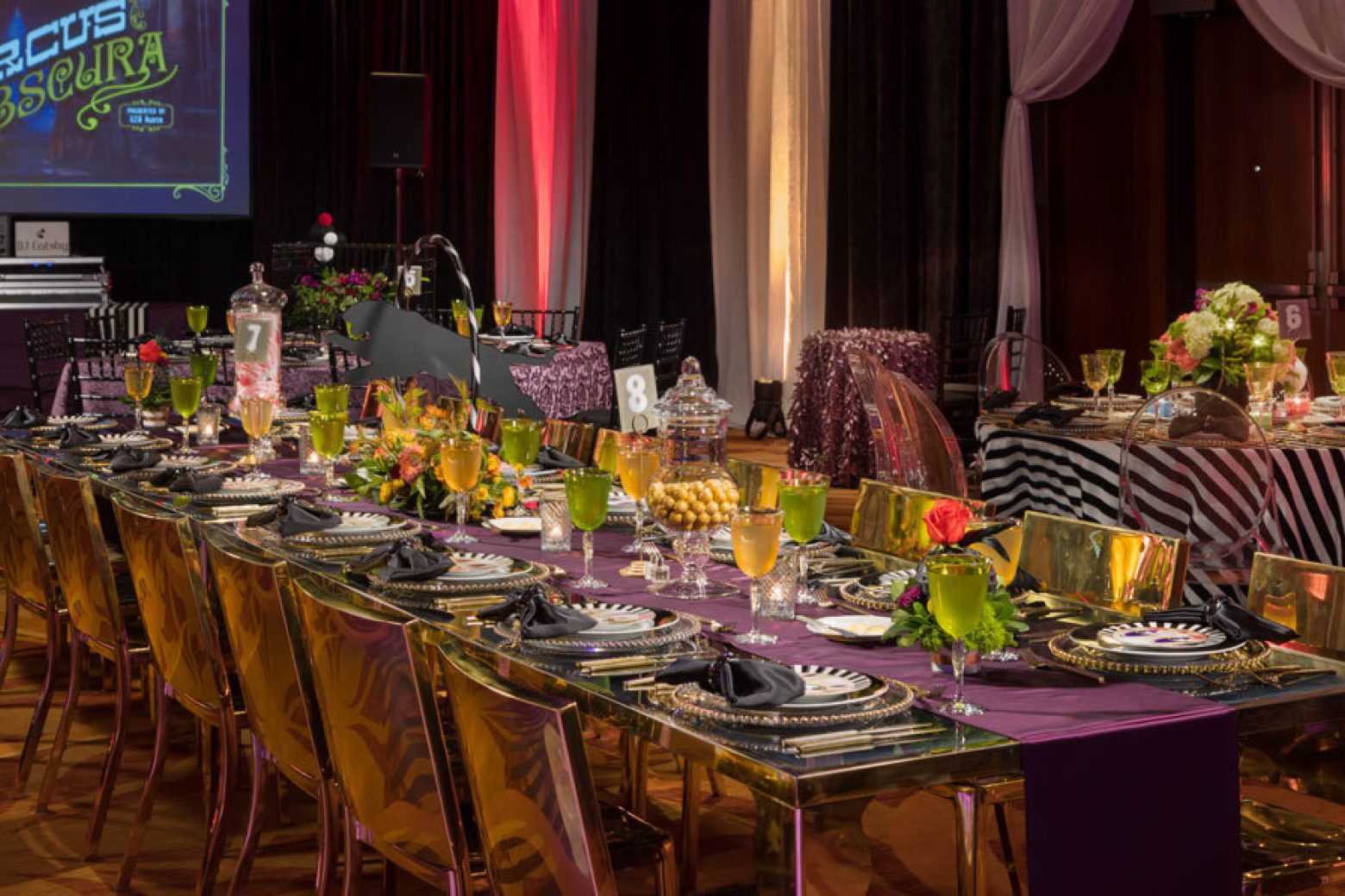 a long table set for a formal event with purple tablecloth, gold chairs, and glasses