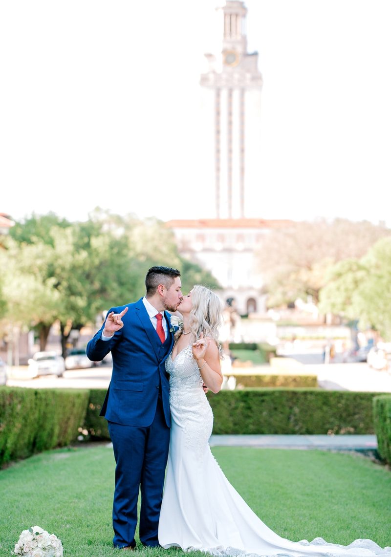 A couple in wedding attire kissing in front of a building with a tower.
