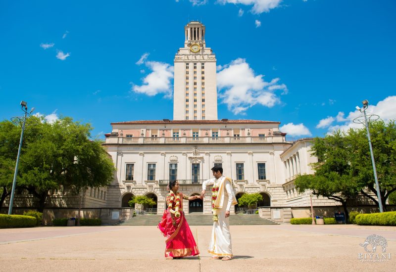A couple in traditional Indian clothing standing in front of a large white building with a clock tower.