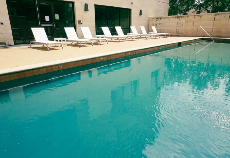 A swimming pool with lounge chairs on the deck and a building in the background.