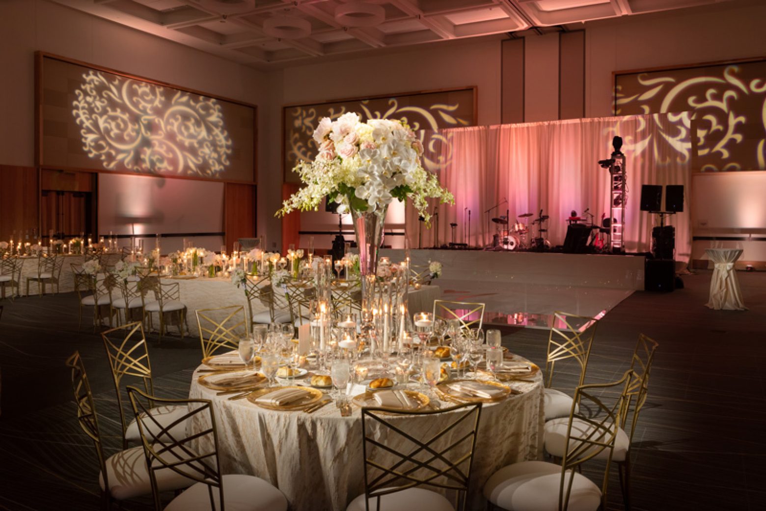 A large, elegantly set dining table in a banquet hall with a stage in the background.