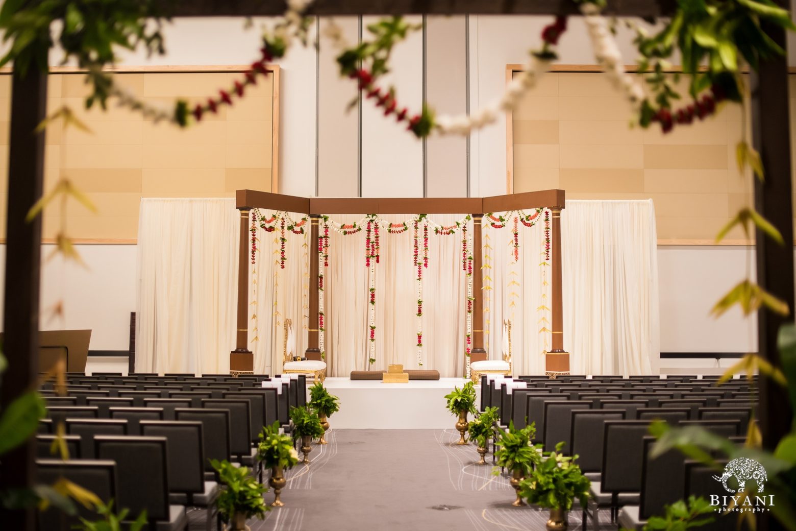 A decorated meeting room with rows of chairs, a stage with curtains and flowers, and an aisle leading to the front.