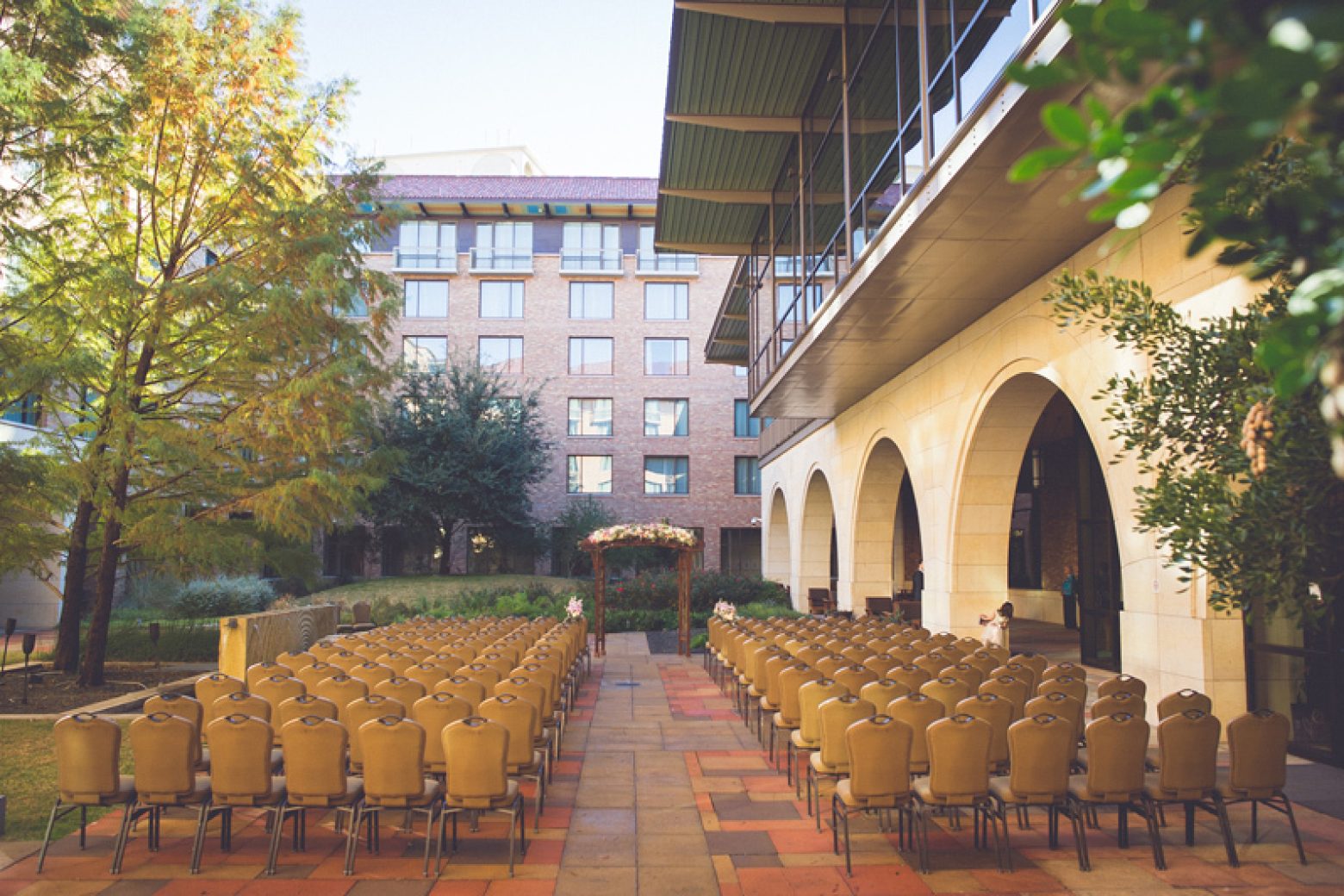 A courtyard with rows of chairs set up for an event, surrounded by a building with arched walkways and balconies.