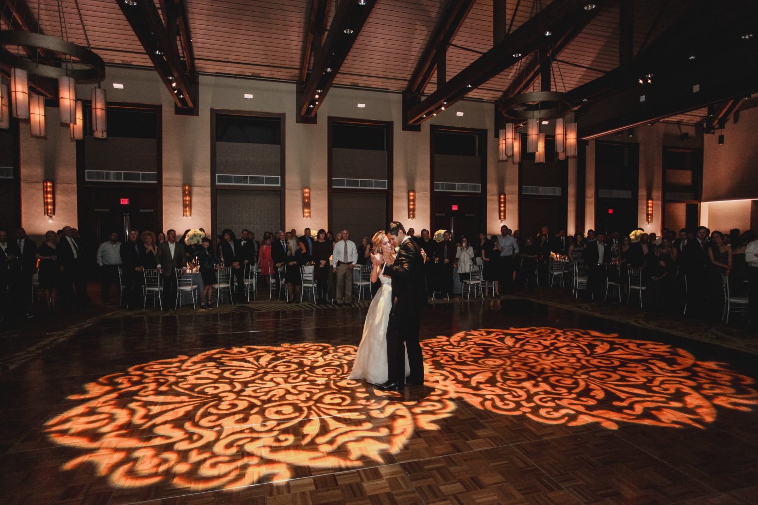 A large room with a high ceiling, filled with people, and a couple dancing in the center.