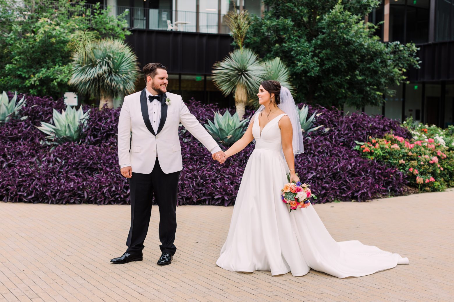 A wedding couple holding hands in the gardens and pathway of a building