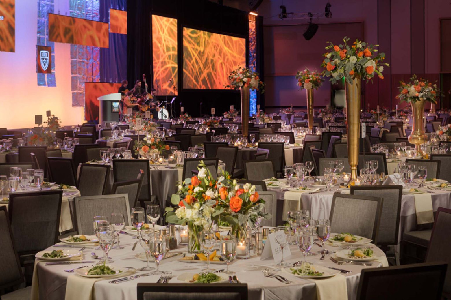 A large, elegantly set dining room with round tables, white tablecloths, and floral centerpieces.