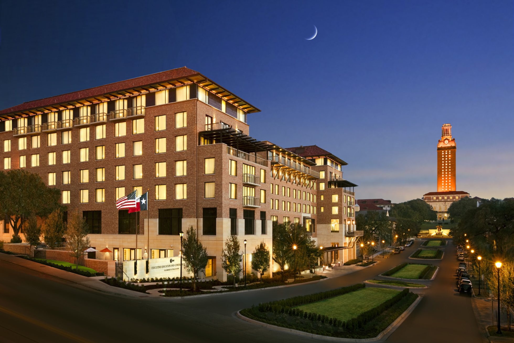 a large brick hotel building with flags and lights on a street corner at dusk