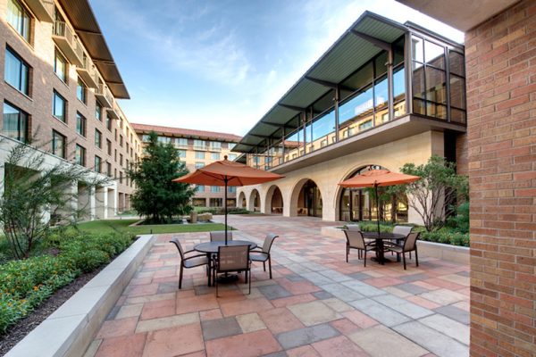 A courtyard with a paved patio, seating areas with umbrellas, and surrounding buildings.