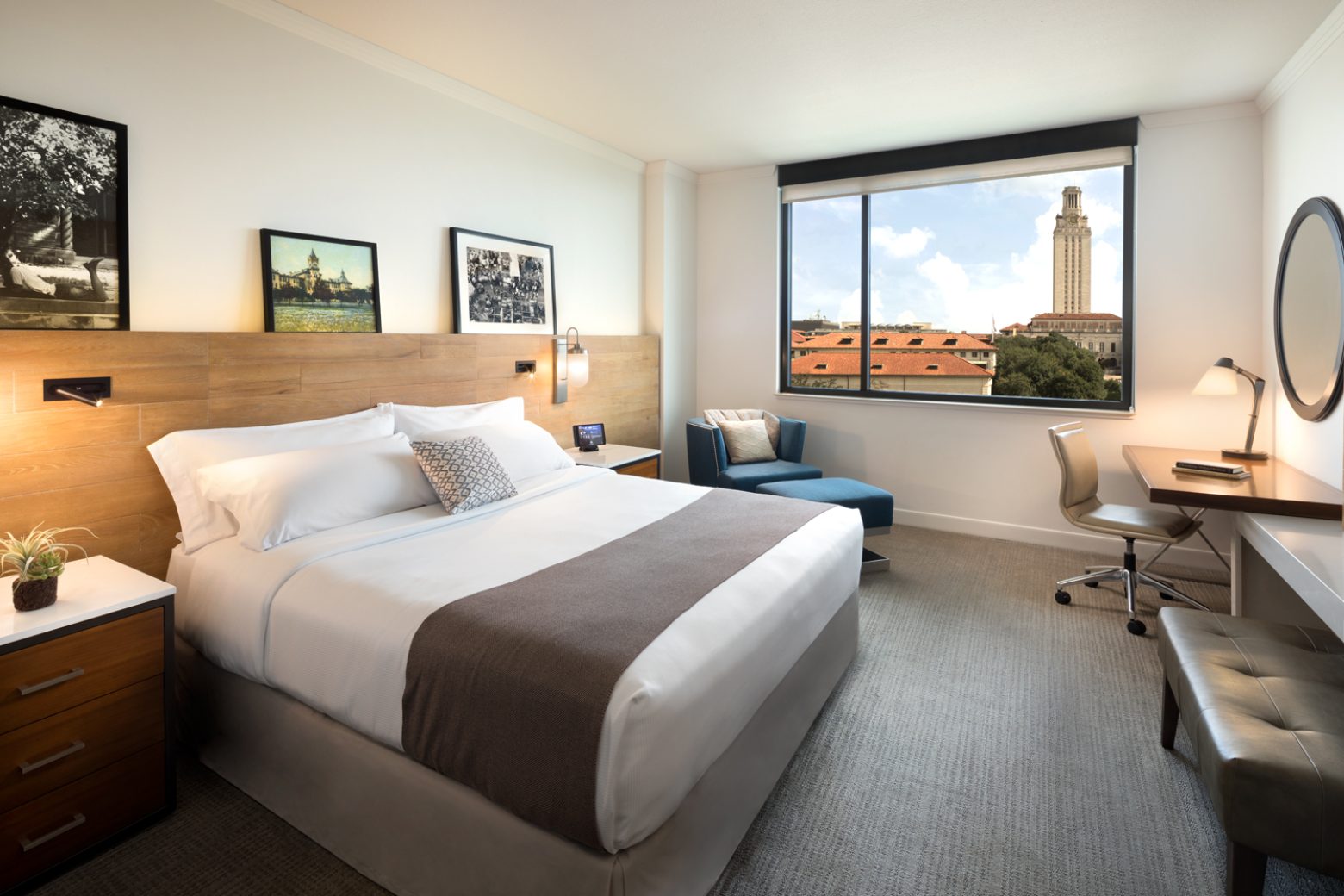 A hotel room with a bed, desk, chair, and window showing a city view.