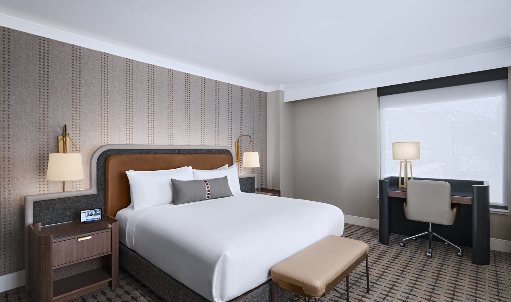 A hotel room with a bed, desk, and window